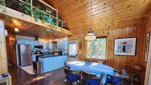 Een houten chalet van binnen met een keuken, eethoek en een balkon met planten.