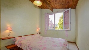 A bedroom with a wooden bed, two bedside lamps, a window with pink curtains, and a view of greenery outside. - 2 bedroom gorgeous apartment in Poggio Di Nazza (Poggio Di Nazza)