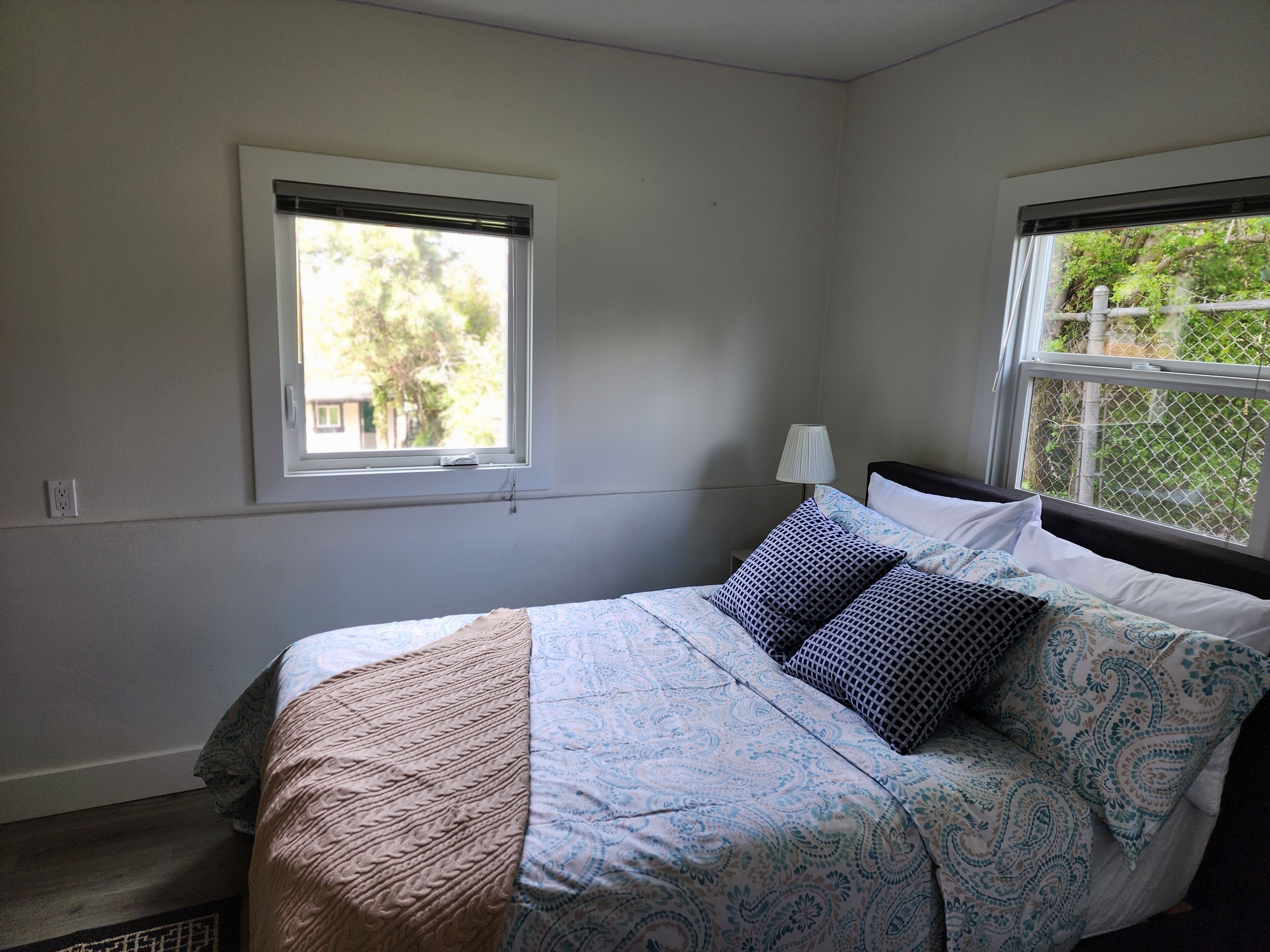 A bedroom with a bed, two windows, a nightstand, and a lamp.