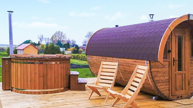 A wooden sauna with a curved roof, a wooden deck, and two wooden chairs.