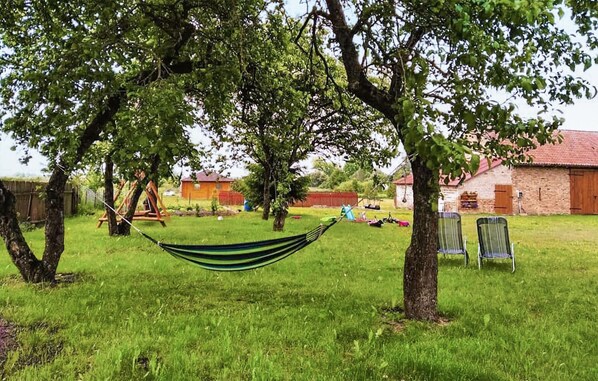 A grassy outdoor area with a hammock, trees, and a brick building in the background.