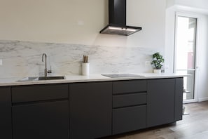 A modern kitchen with a marble backsplash, a stainless steel sink, and a black range hood.
