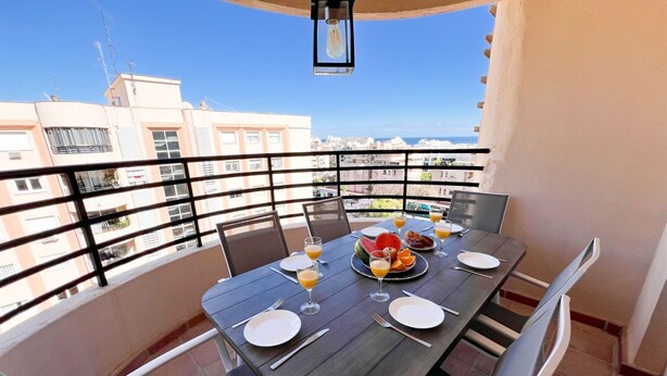 Un balcon avec une table mise pour le petit-déjeuner, comprenant des assiettes, des verres et un panier de fruits.