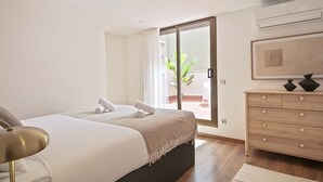 Une chambre à coucher comprenant un lit, une commode, une chaise et une porte-fenêtre coulissante donnant sur un balcon.