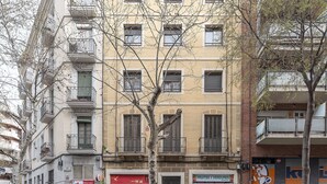 Une vue de rue avec une épicerie proposant des fruits et légumes, une pharmacie et une rangée d’immeubles d’habitation.