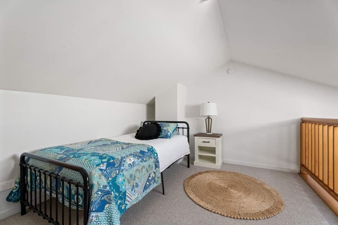 Een slaapkamer met een bed, nachtkastje, lamp en een klein vloerkleed.