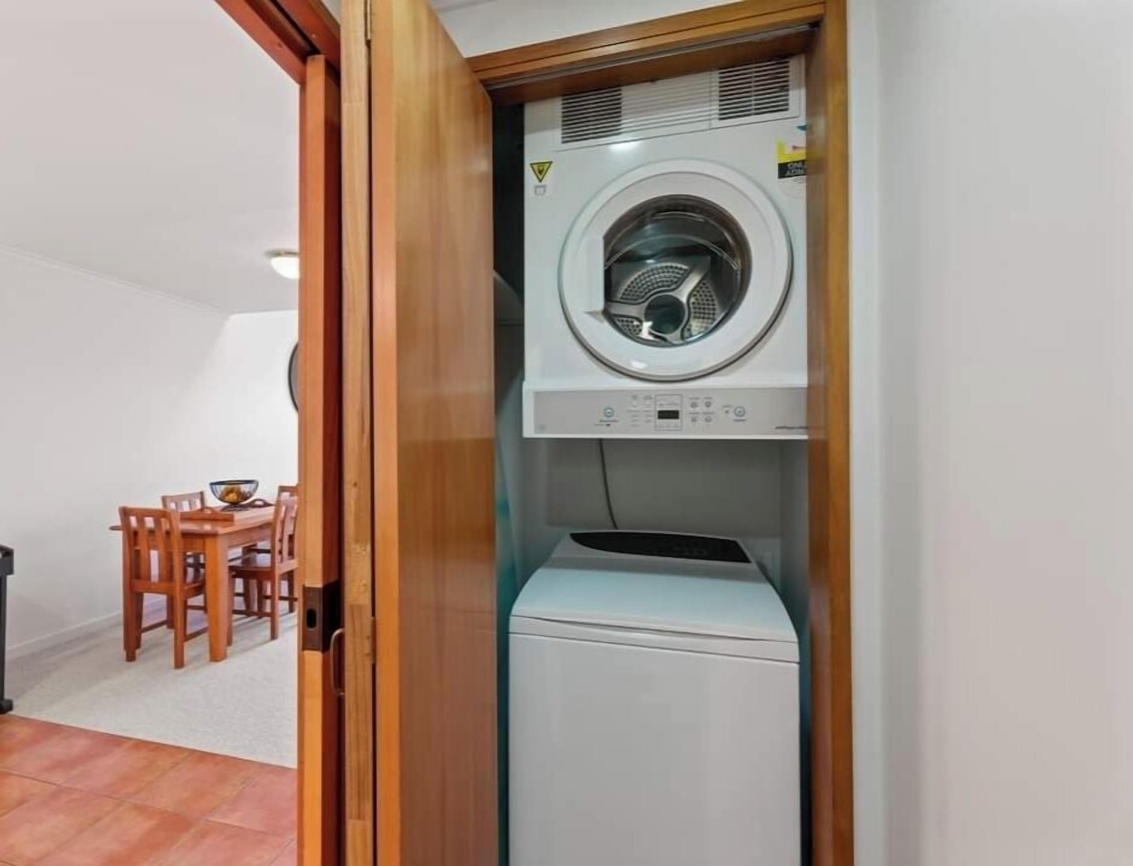 Une petite buanderie équipée d’un lave-linge et d’un sèche-linge à chargement frontal, d’un cadre de porte en bois et d’un petit coin repas avec une table et des chaises.