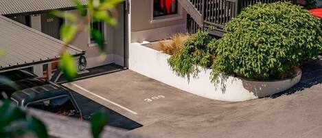 Um espaço de estacionamento com um carro, um edifício com escadas e um arbusto bem cuidado.