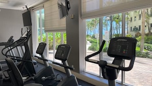 Une salle de sport équipée de tapis de course et d’appareils de musculation, de grandes fenêtres offrant une vue sur des palmiers et un immeuble.