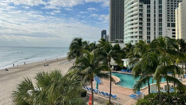 Un hôtel doté d’une piscine, offrant une vue sur la plage et bordé de palmiers.