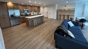 Une cuisine moderne dotée d’appareils électroménagers en acier inoxydable, un îlot central avec des tabourets, et un espace de vie avec un canapé bleu et une table basse.