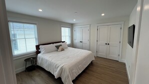 Une chambre avec un grand lit, deux fenêtres, une porte et une petite table.