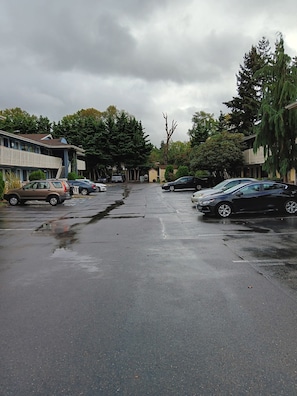 A parking lot with multiple cars, a building with a sloped roof, and trees in the background.