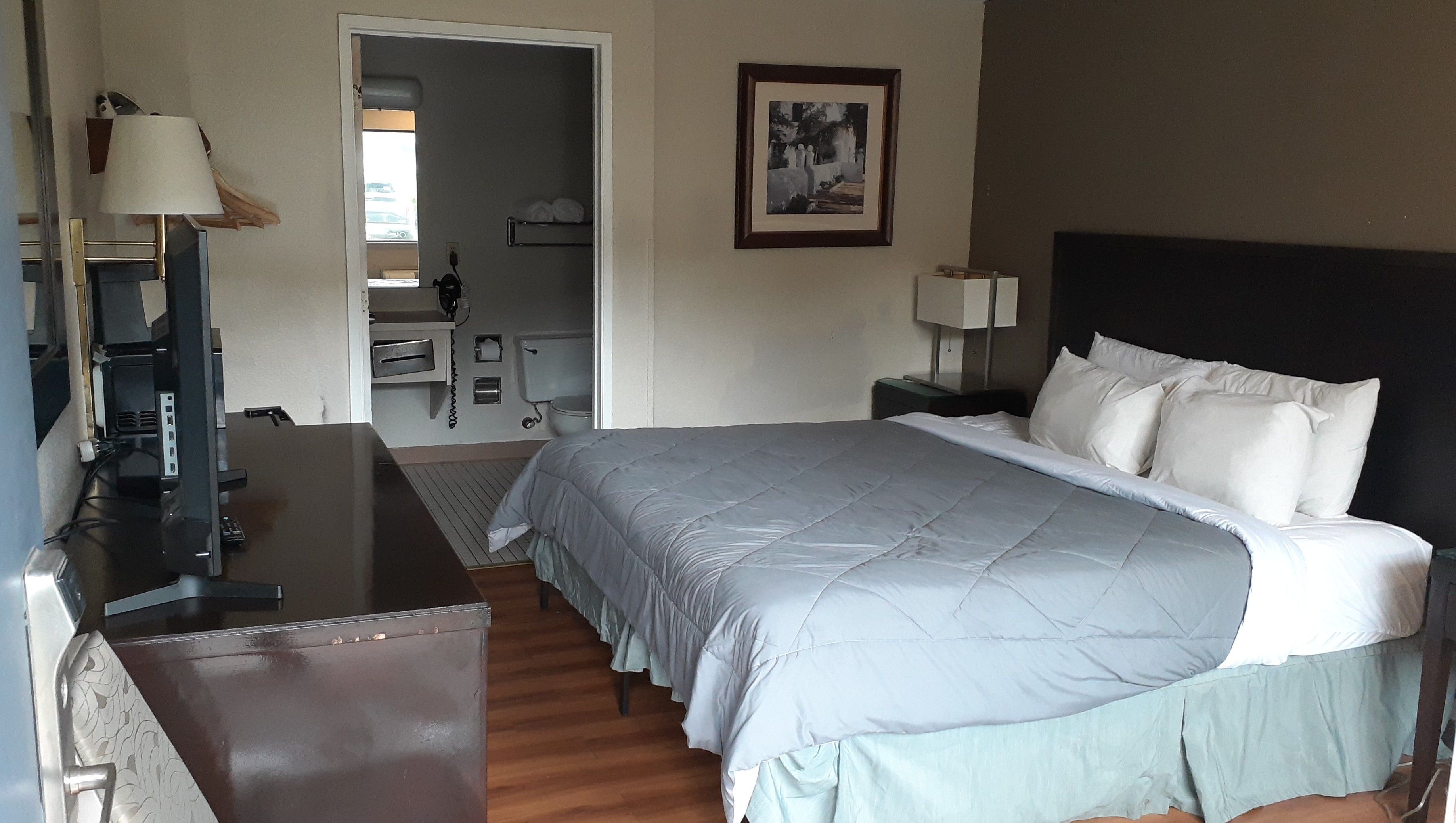 A hotel room with a bed, a desk, a television, a bathroom, and a framed picture on the wall.