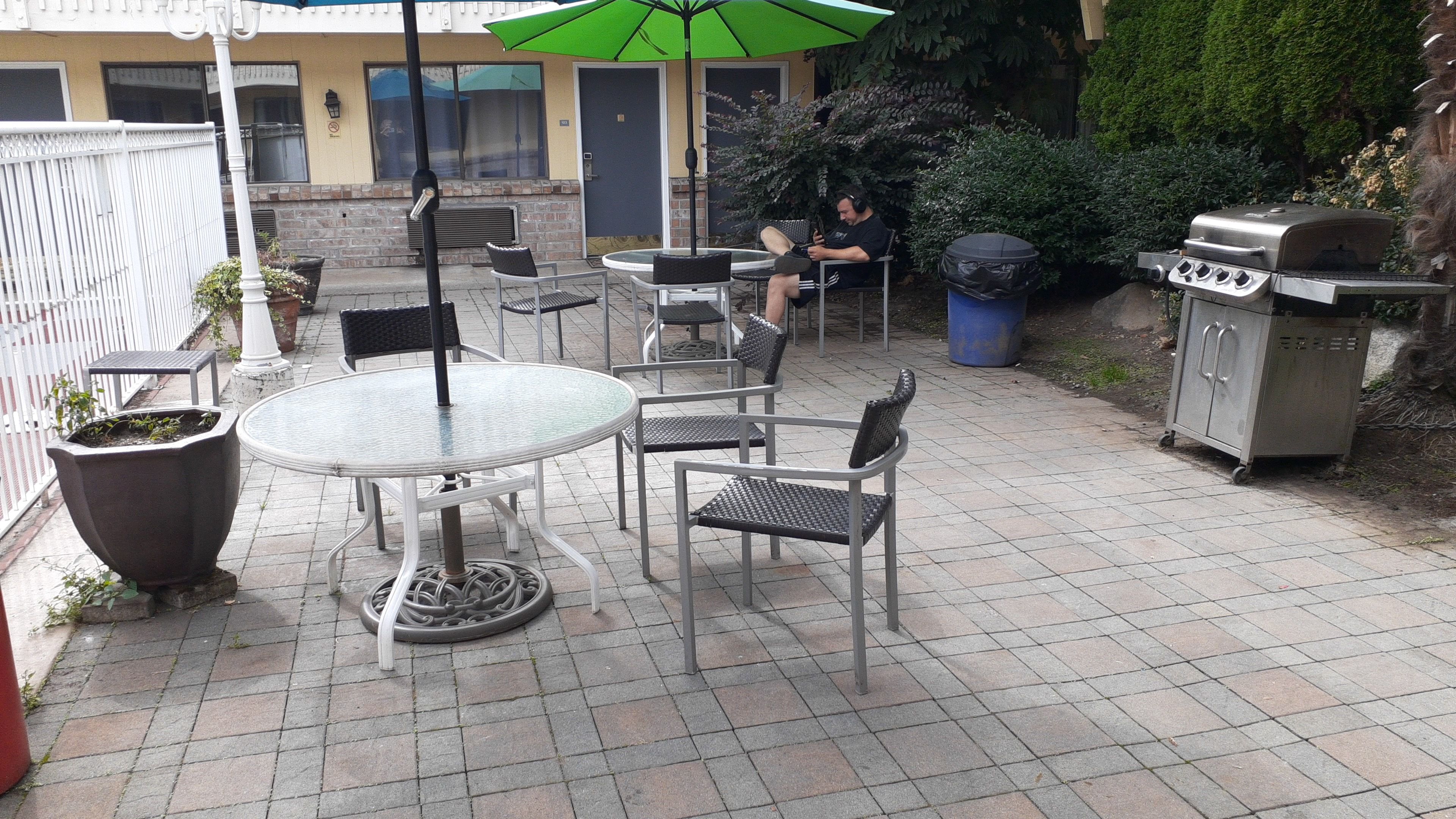 An outdoor patio with a round table and chairs, a grill, and a trash bin.