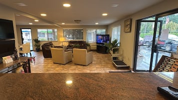 A hotel lobby with a flat-screen TV, leather sofas, a coffee table, and a reception desk with a plant.