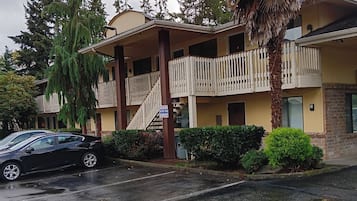 A two-story building with a balcony, a palm tree, and a black car parked in front.