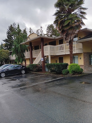 A two-story building with a balcony, a palm tree, and a black car parked in front.
