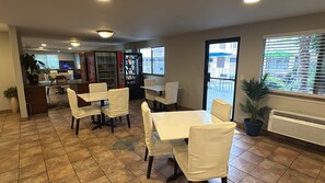 A dining area with white tables and chairs, a vending machine, and a view of the outside through a sliding door. - Seattle Value Inn Near Tacoma Airport I-5 (Tukwila)