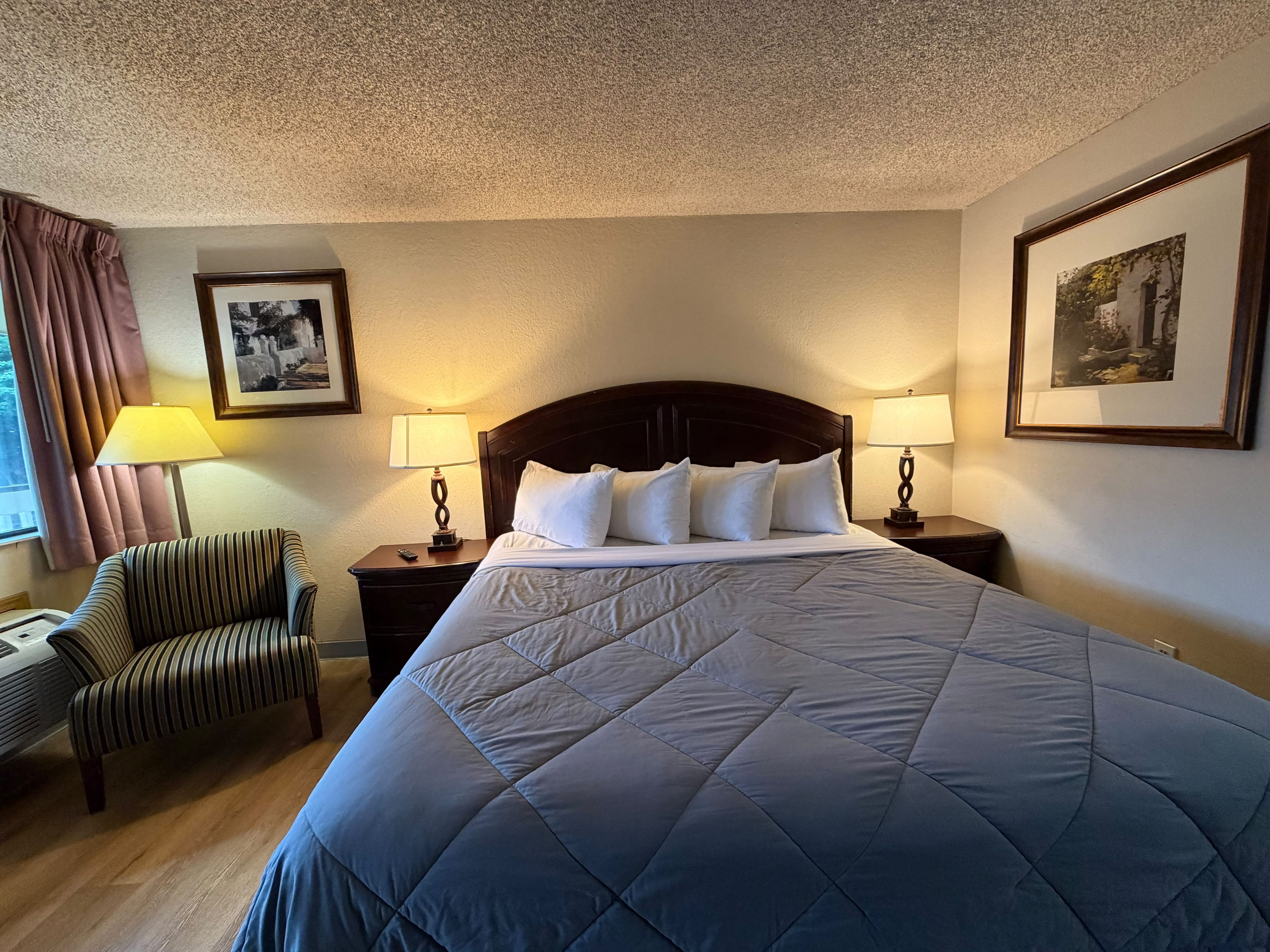 A hotel room with a large bed, two bedside tables with lamps, a chair, and framed pictures on the walls.