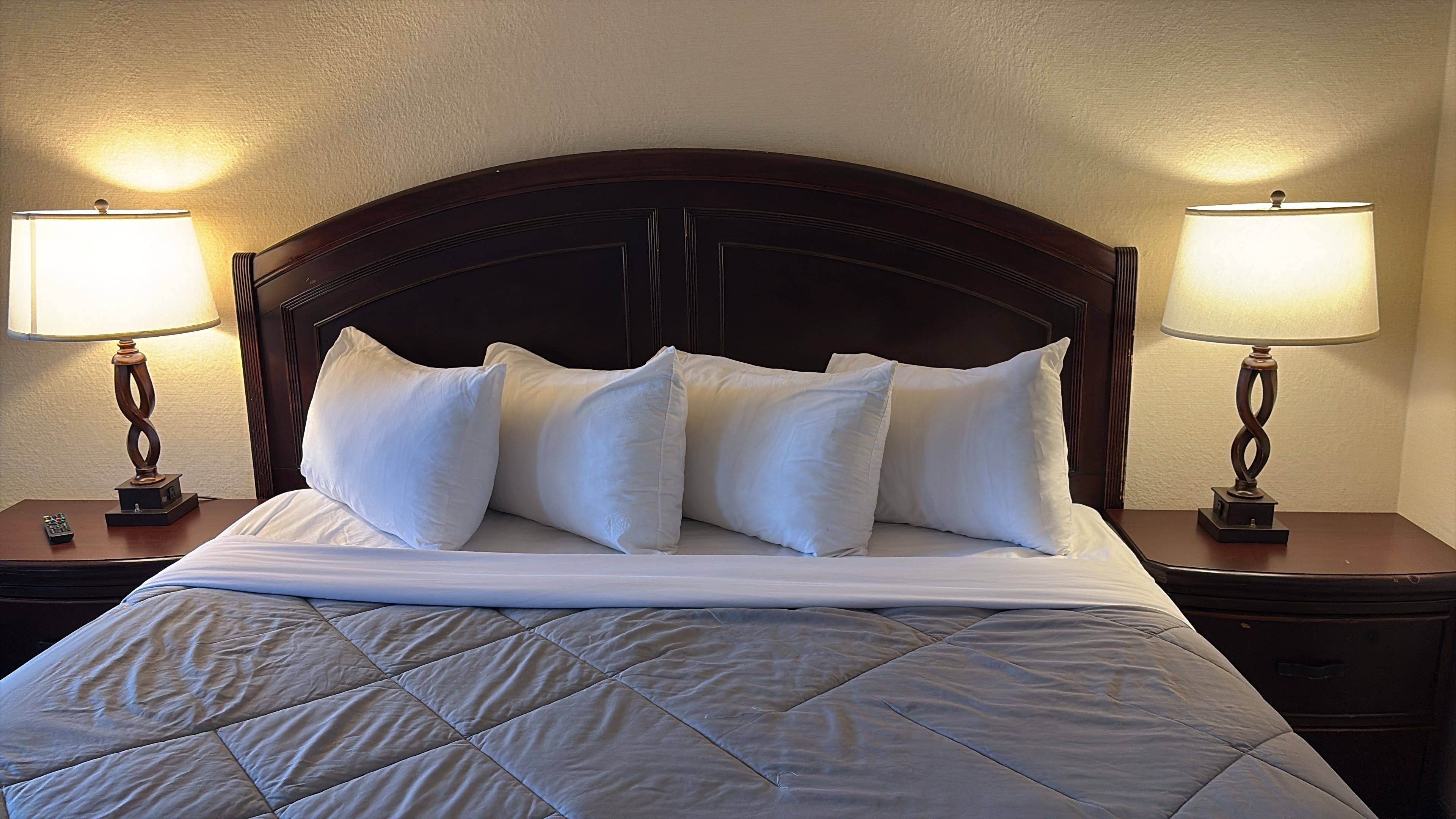 Un lit bien fait, recouvert d’une courtepointe matelassée, avec deux lampes de chevet placées de part et d’autre sur des tables de nuit en bois.