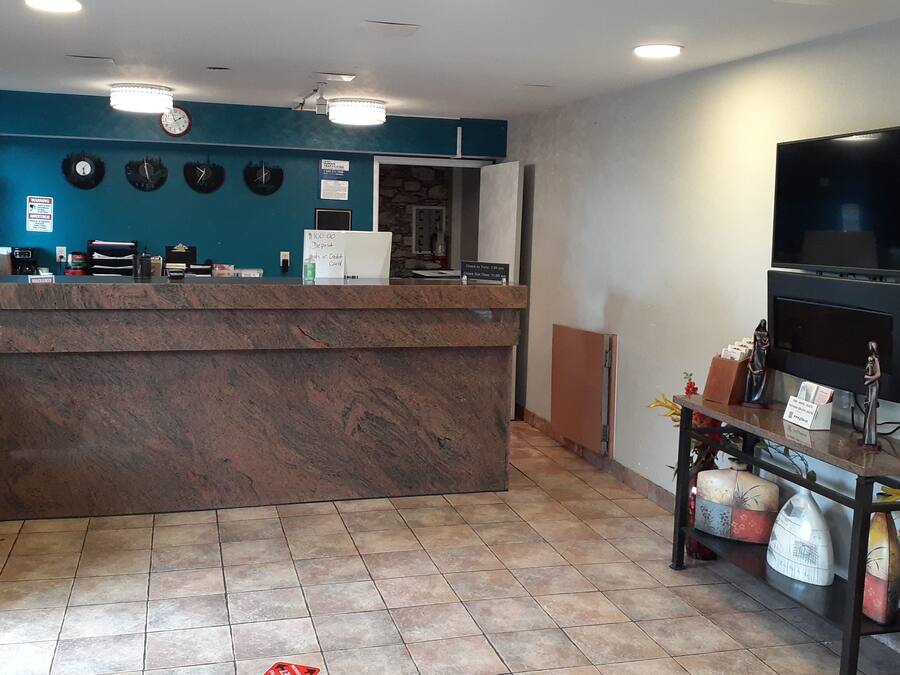 A reception area with a marble counter, clocks, a television, and a vase with flowers.