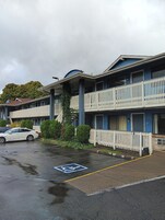 Un motel de varios pisos con estacionamiento, un espacio para discapacitados y una cerca de piquetes blancos.