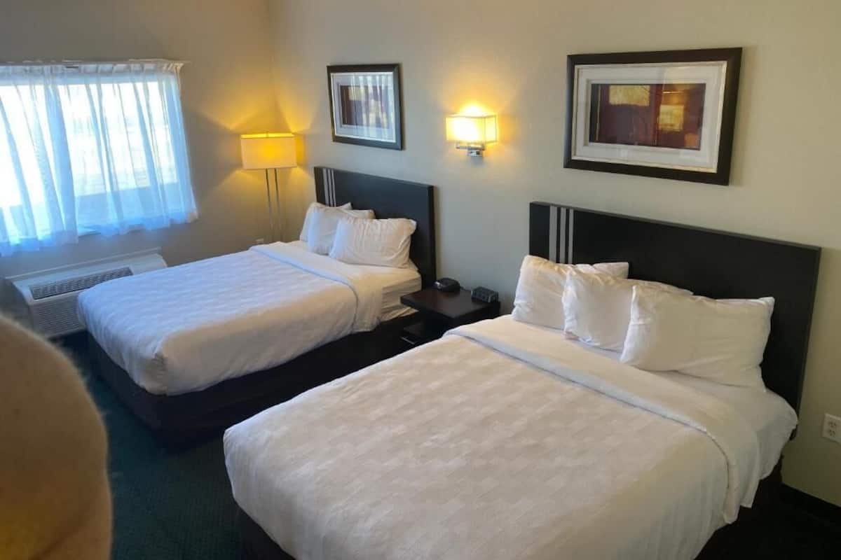 A hotel room with two beds, a window with sheer curtains, a wall-mounted lamp, and framed artwork.