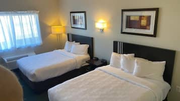 Habitación de hotel con dos camas, una ventana con cortinas traslúcidas, una lámpara de pared y obras de arte enmarcadas.