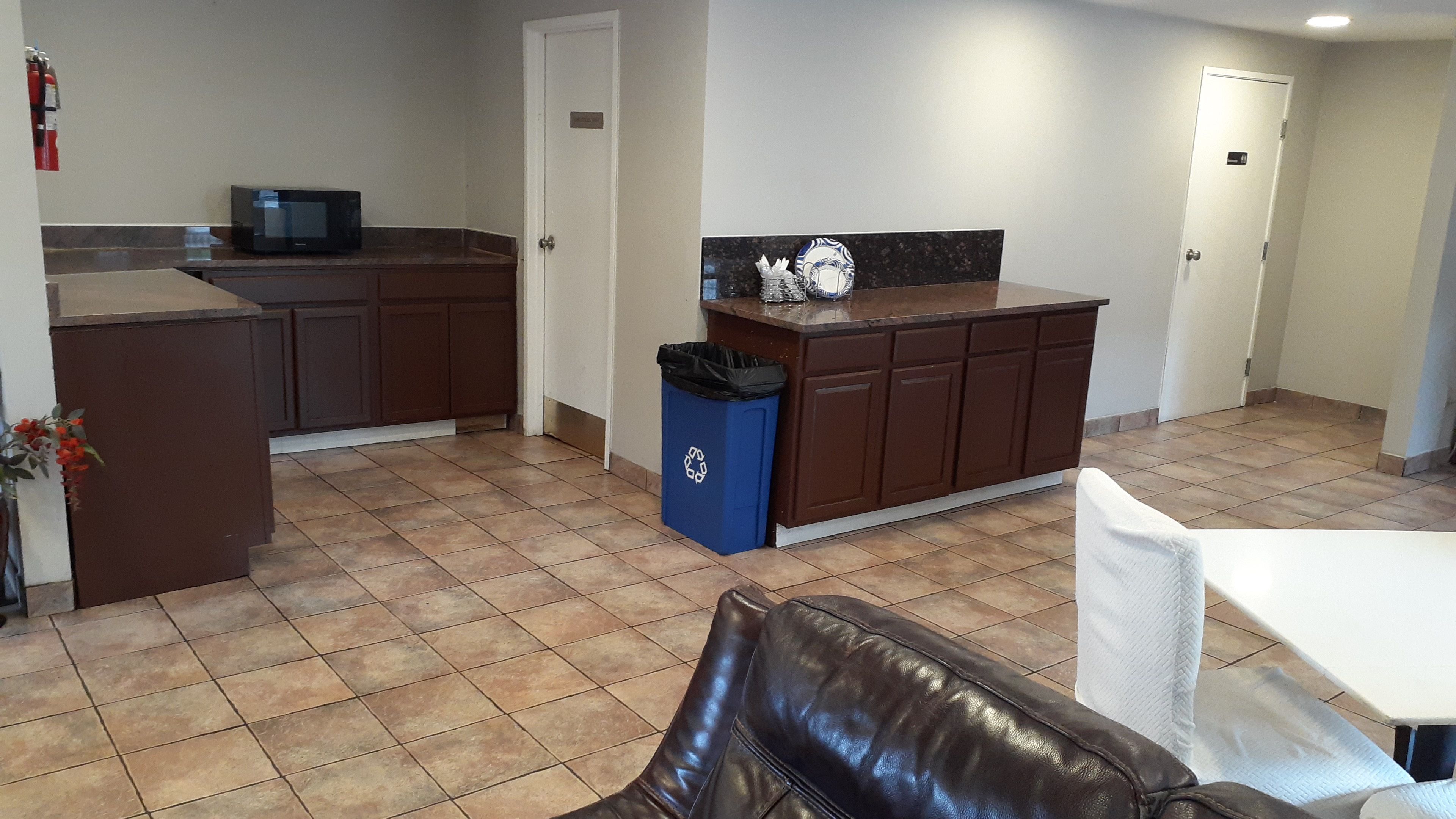 A kitchen with brown cabinets, a microwave, and a trash bin.