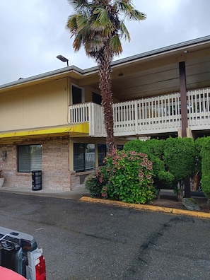 A two-story building with a balcony, a palm tree, and a flower bed.