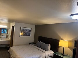 Una habitación de hotel con cama, mesita de noche, lámpara y un cuadro en la pared.