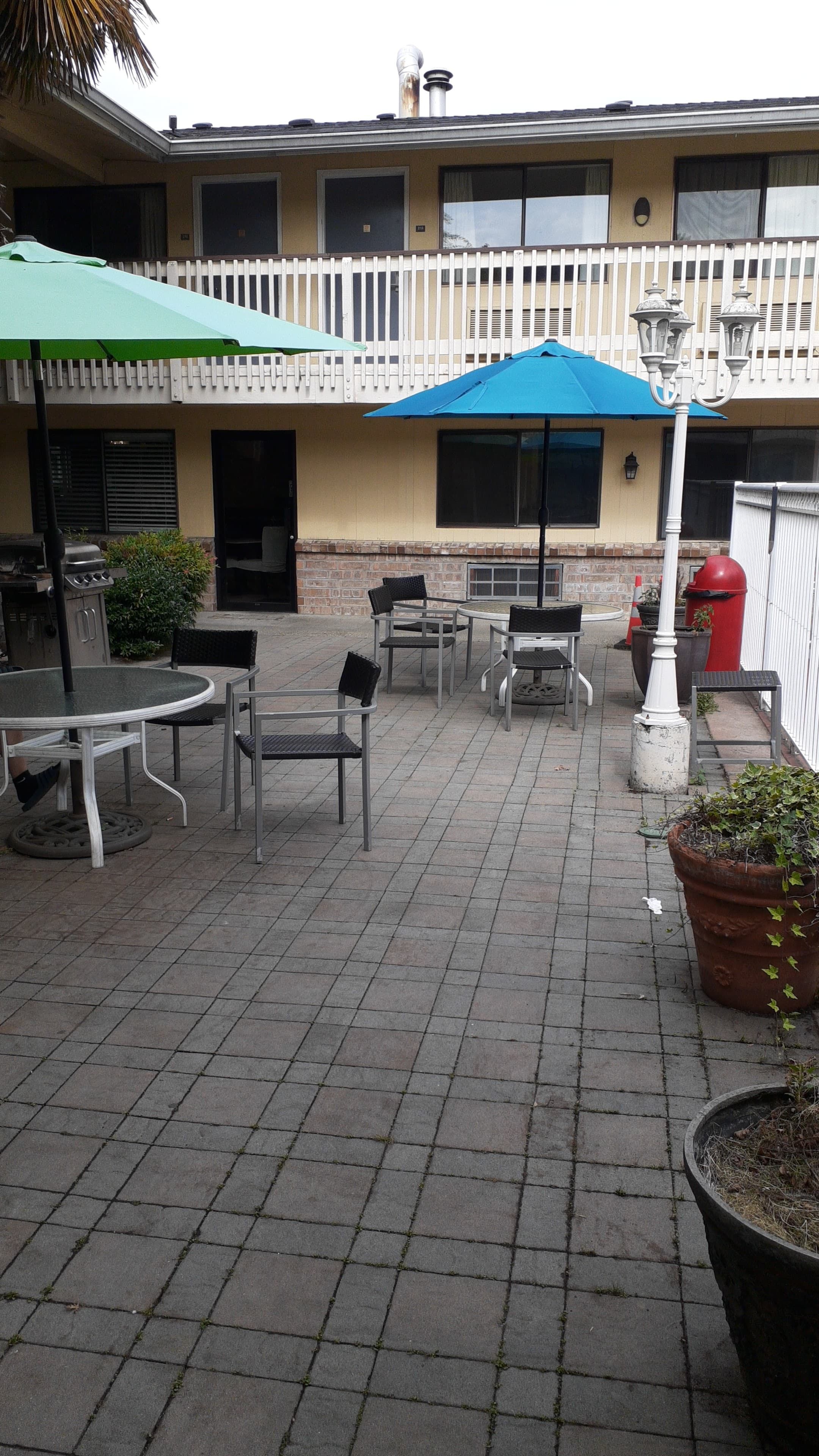An outdoor patio area with tables and chairs, a barbecue grill, and umbrellas.