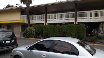 A parking area with a building featuring a balcony with a white railing.