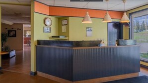 A reception desk with a dark counter, pendant lights, framed certificates on the wall, and a view of the outdoors through a large window. - Hotel Viewmont Residency Ltd. (Logan Lake)