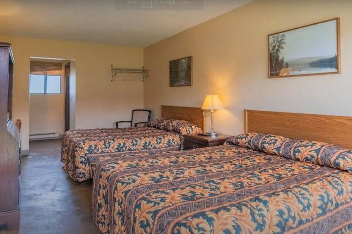 A hotel room with two beds, a desk, a chair, a lamp, and a painting on the wall.