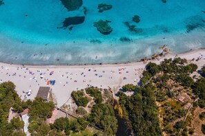 An aerial view of a beach with clear turquoise water, sandy shore, and scattered beach umbrellas.