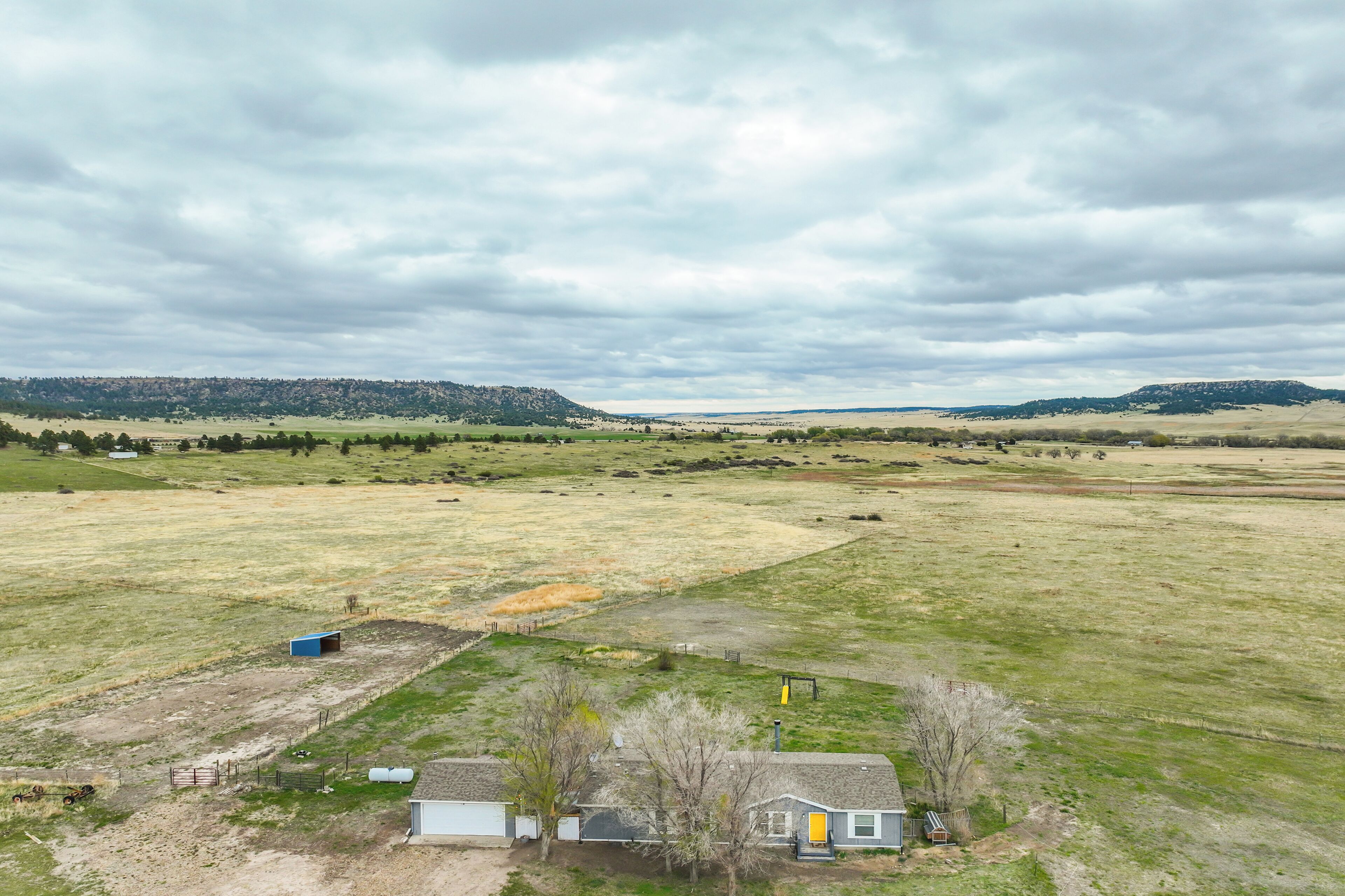 A rural landscape with a small house, a fenced yard, and distant hills.