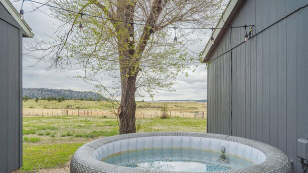 A hot tub in a covered outdoor area with a view of a grassy field and hills in the background. - Hawkeye (Peyton)