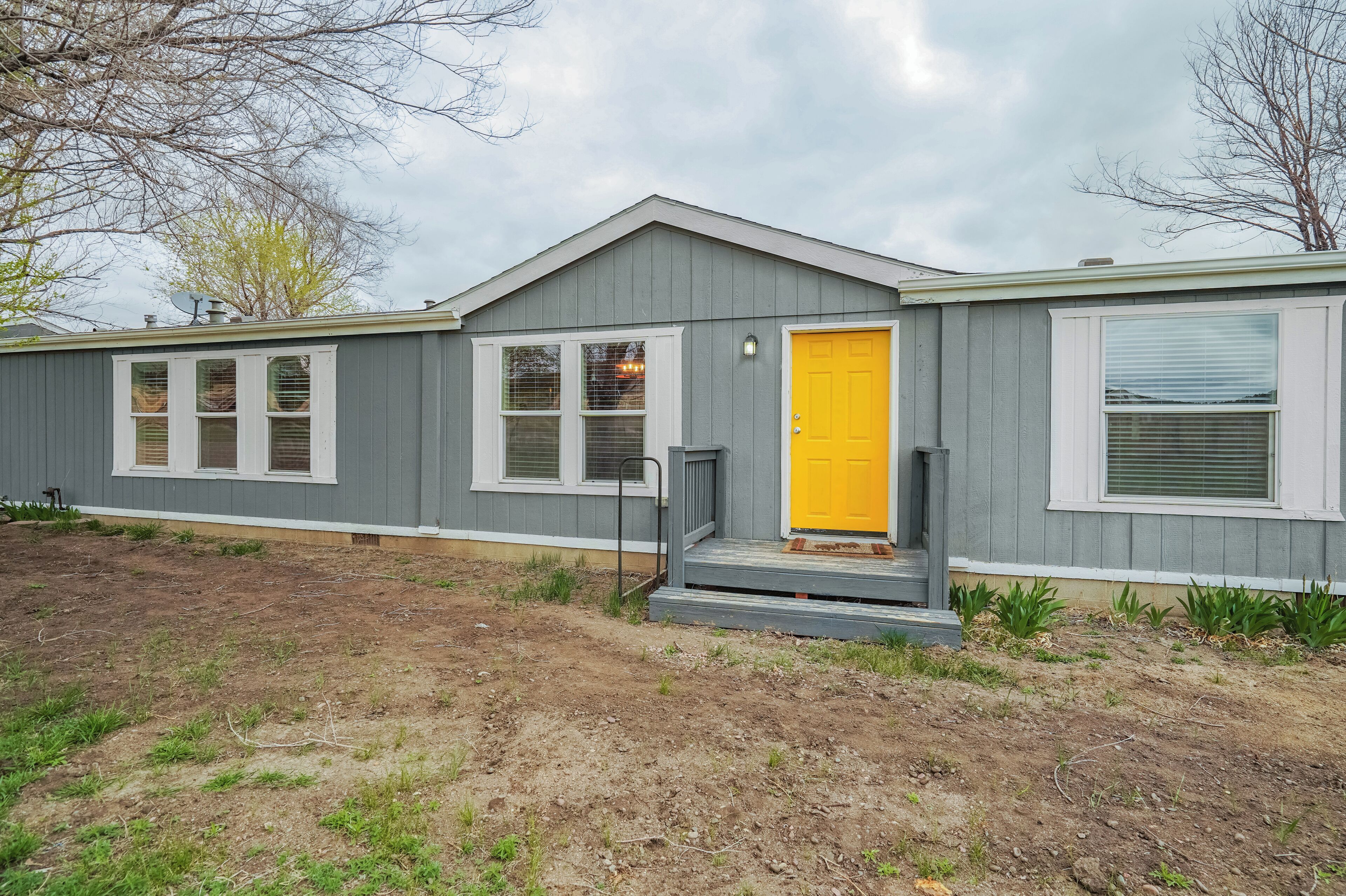 A single-story house with a gray exterior, a yellow front door, and a small porch.