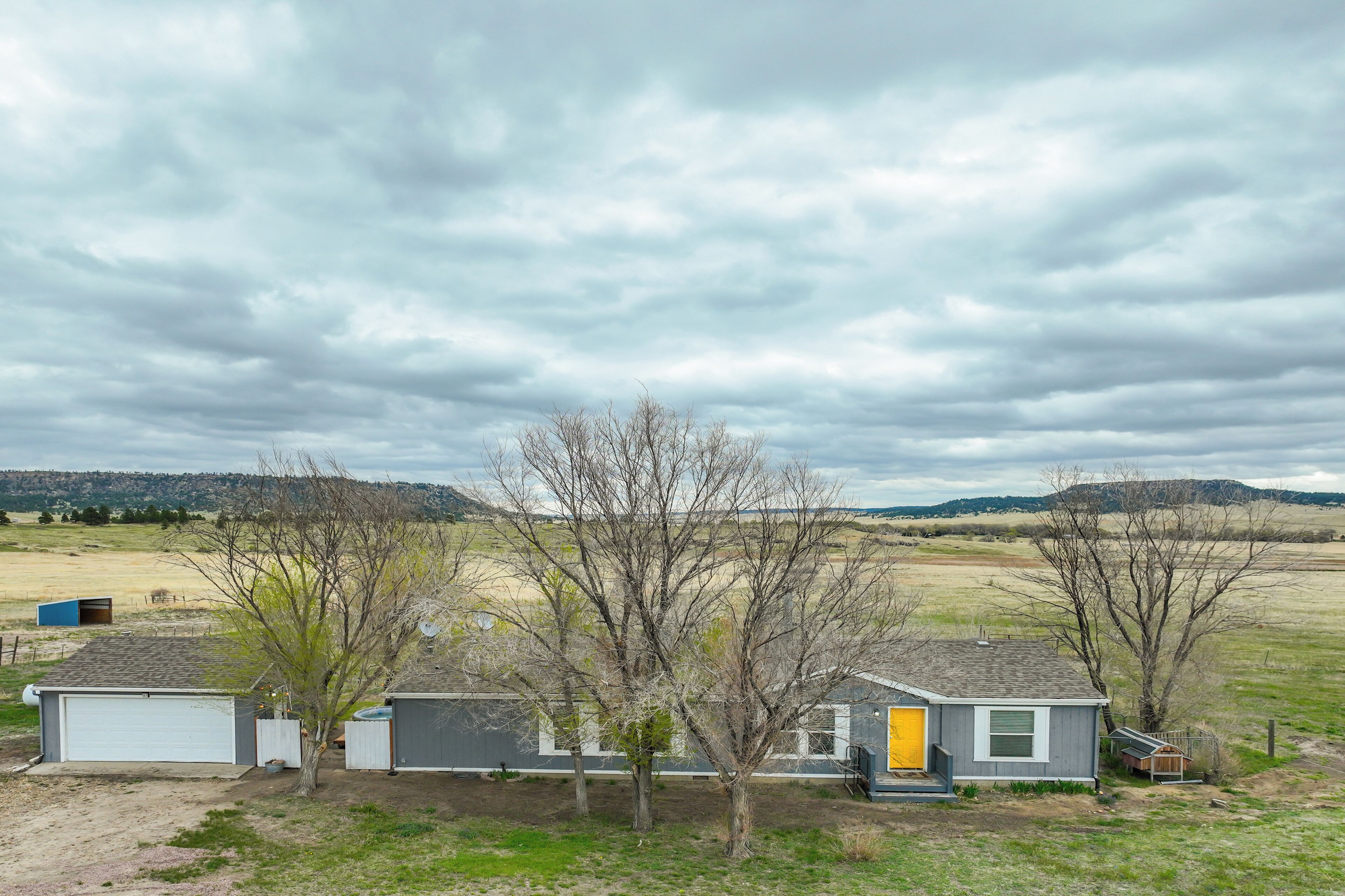 A rural property with two detached houses, one with a yellow door, surrounded by open fields and a cloudy sky.