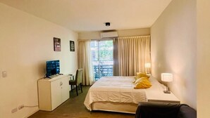 Ein Hotelzimmer mit Bett, Schreibtisch, Stuhl, Fernseher und einem Balkon mit Vorhängen.