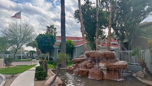 A landscaped area with a water feature, palm trees, and a building with a red-tiled roof. - Modern, Cozy Condo in North PHX with Pool in Gated Community! (Phoenix)