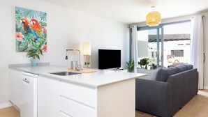 Een moderne keuken met een centraal eiland, een flatscreen televisie en een zithoek met een grijze bank.