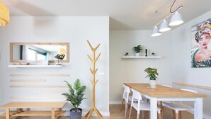 Een moderne eetruimte met een houten tafel, witte stoelen, een bankje, een kapstok en een potplant.