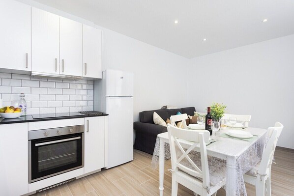 Een moderne keuken met witte kasten, een inbouwoven en een eethoek met een tafel voor twee personen.