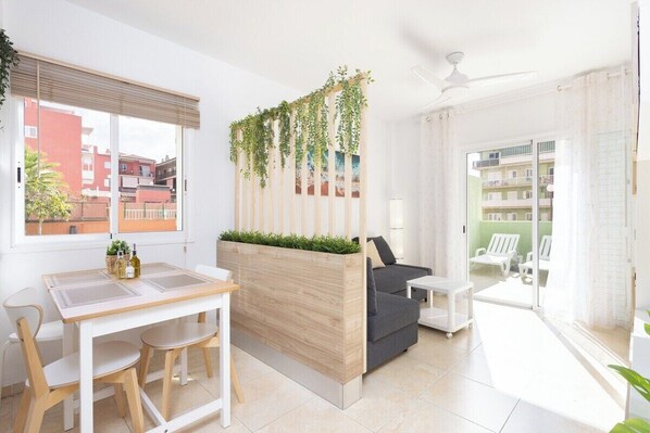 A modern living room with a wooden partition, a dining table with chairs, a sofa, and a balcony with white chairs.