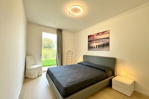 Un dormitorio moderno con cama, mesita de noche con lámpara, ventana con cortinas y un cuadro en la pared.