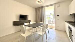 Een moderne keuken met een ingebouwde oven, een eethoek met een donker houten tafel en witte stoelen, en een schuifdeur naar een terras.