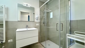 Une salle de bain moderne avec une douche à l’italienne en verre, un meuble-lavabo blanc et un miroir.
